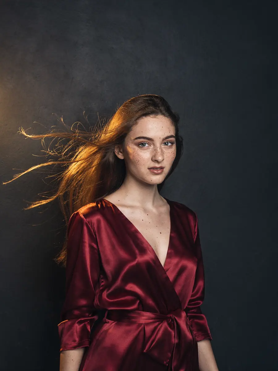 A photograph of a woman in a red silk dress against a dark wall